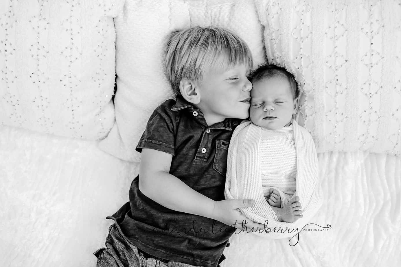 brother and baby sister cuddling in bed during photo session pensacola fl